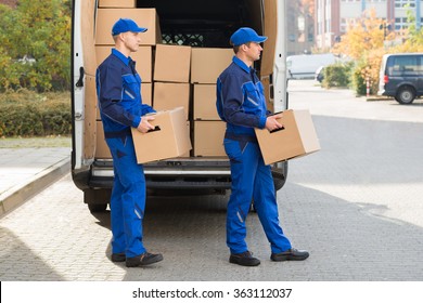 Smiling Young Delivery Men Carrying Cardboard Boxes While Walking Outside Truck