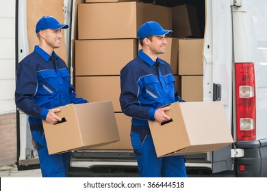 Smiling Young Delivery Men Carrying Cardboard Boxes While Walking Outside Truck