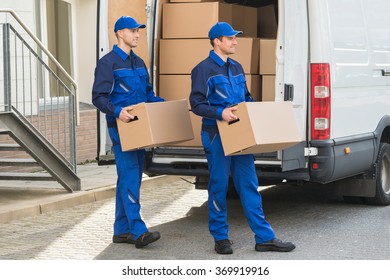 Smiling Young Delivery Men Carrying Cardboard Boxes While Walking Outside Truck