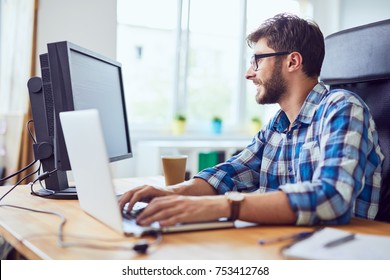 Sorrindo jovem desenvolvedor digitando código no laptop e olhando para a tela no escritório