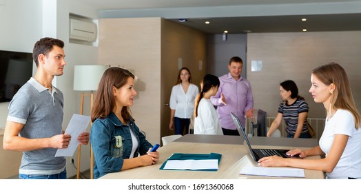 Smiling Young Diligent Positive Cheerful Woman Assistant Of Notary Public Receiving Customers In Hall Of Modern Office 