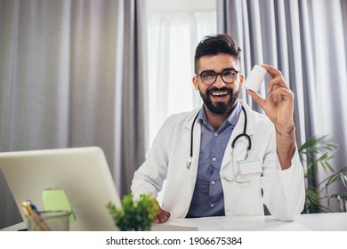 Smiling young doctor patient, using laptop, looking at camera, sitting at desk in office.