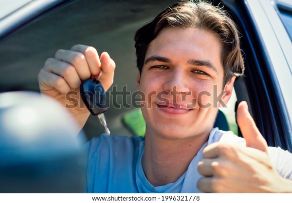 Smiling young\
driver showing new car keys and\
car.