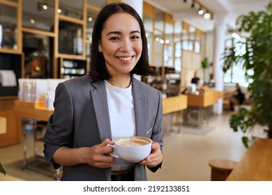 Smiling young elegant professional leader Asian woman, female executive manager businesswoman, coffee house small business owner wearing suit holding coffee standing looking at camera, portrait.