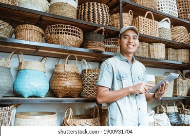 smiling young entrepreneur looking at the camera while holding a digital tablet while standing with a hand-crafted bag in the background - Powered by Shutterstock