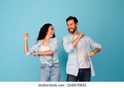 Smiling young european guy and middle eastern lady in casual have fun together, dance, isolated on blue background, studio. Entertainment, couple enjoy free time, offer and ad, reaction on good news - Shutterstock ID 2240570833