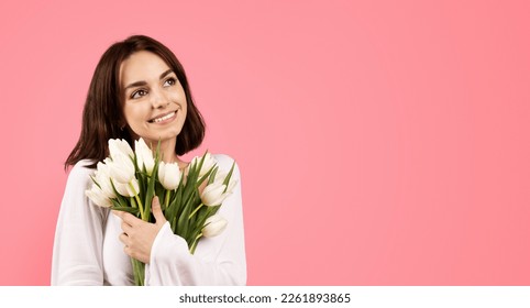 Smiling young european lady hug bouquet of white tulips to chest, looks at empty space, enjoy spring holiday, isolated on pink background, studio. Gift to women day, congratulation, anniversary, date - Shutterstock ID 2261893865