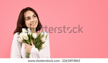 Smiling young european lady hug bouquet of white tulips to chest, looks at empty space, enjoy spring holiday, isolated on pink background, studio. Gift to women day, congratulation, anniversary, date