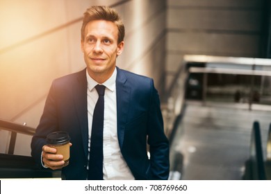 Smiling young executive in a suit drinking a coffee and riding up an escalator in a subway station during his morning commute - Powered by Shutterstock