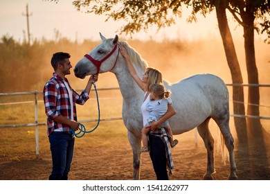 Smiling Young Family In A Horse Farm Petting Horses 