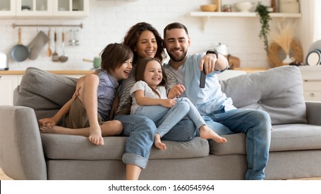 Smiling young family with little preschooler kids sit on couch in kitchen make self-portrait picture on cell together, happy parents with small children have fun take selfie on smartphone at home