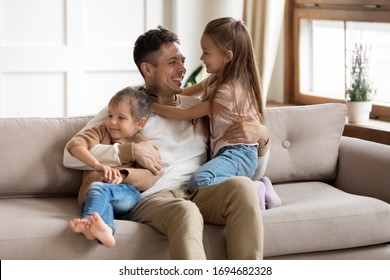 Smiling young father sitting on comfortable couch, playing with small cute kids daughters in living room. Happy uncle having fun communicating entertaining with little adorable children nephews. - Shutterstock ID 1694682328