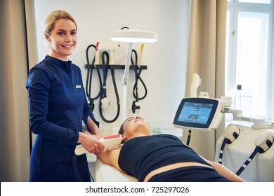 Smiling young female beautician performing an electrolysis hair removal procedure on the underarm of a woman lying on a table in a beauty clinic