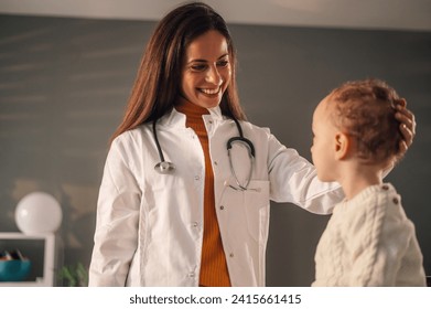 Smiling young female doctor or pediatrician examining small boy patient at consultation in private clinic. Doctor at home service. Focus on a woman doctor. - Powered by Shutterstock