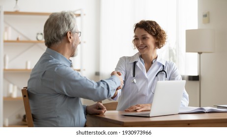 Smiling young female doctor shake hand close health insurance deal with elderly patient at consultation in hospital. Happy woman GP handshake greeting get acquainted with mature man in clinic.