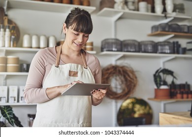 Smiling young female florist standing in her flower shop checking online orders with a digital tablet - Powered by Shutterstock