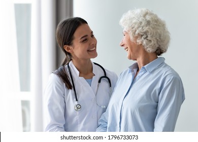 Smiling young female general practitioner enjoying sincere talk, sharing good health news with hoary older senior woman indoors. Caring millennial nurse helping middle aged patient at meeting.
