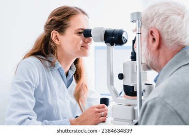 Smiling young female oculist checking senior patient`s vision with ophthalmic equipment, modern apparatus, slit-lamp, retinoscope in clinic hospital - Powered by Shutterstock