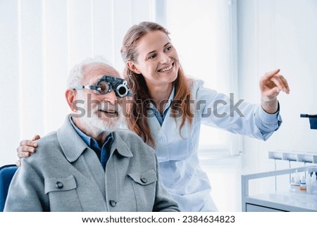 Smiling young female oculist helping her aged male patient checking sight using spectacles. Caucasian female optometrist selecting glasses eye lenses for senior man