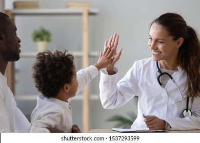 Smiling Young Female Pediatrician Give High Five To Little African American Boy At Consultation In Clinic, Happy Woman Doctor Consult Biracial Toddler Kid In Hospital. Children Healthcare Concept