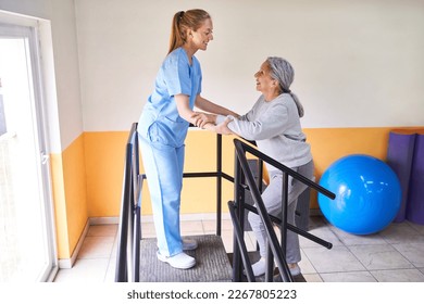 Smiling young female physiotherapist assisting elderly woman in climbing ramp at rehabilitation center - Powered by Shutterstock