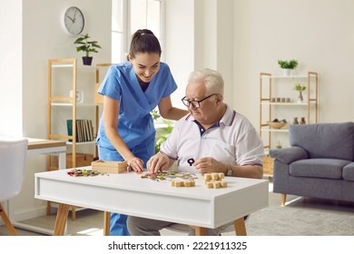 Smiling young female social worker and old man playing with jigsaw puzzle in nursing home. Caregiver in medical uniform helps elderly man to put together puzzles and letters. Old age concept. - Powered by Shutterstock