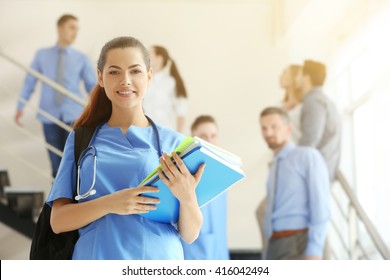 Smiling young female student with backpack and books, indoors