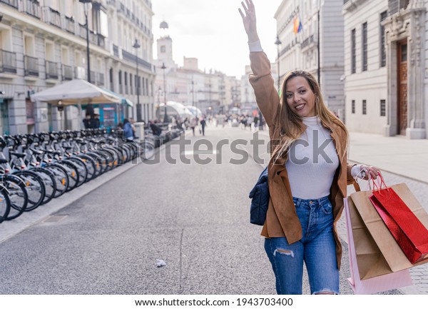 Smiling young female tourist waiting for cab\
outdoors. Cheerful modern lady with bag gesturing to give signal to\
taxi driver. Taxi service\
concept