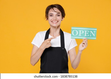 Smiling Young Female Woman 20s Barista Bartender Barman Employee In White T-shirt Apron Posing Pointing Index Finger On Sign With OPEN Title Isolated On Yellow Color Wall Background Studio Portrait