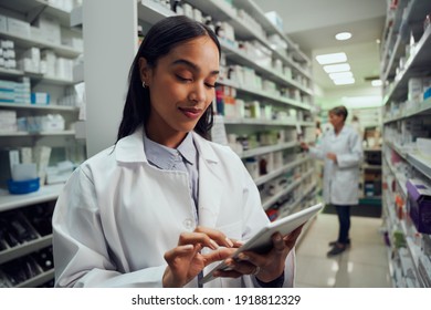 Smiling young female worker in pharmacy wearing labcoat checking inventory using digital tablet - Powered by Shutterstock