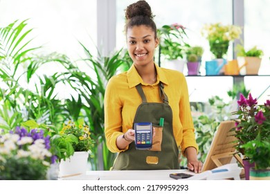 Smiling young florist holding a POS terminal and looking at camera, electronic payments concept