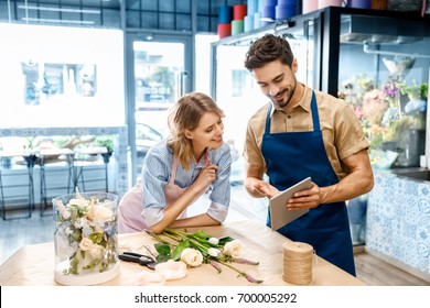 smiling young florists in aprons using digital tablet while working together in flower shop - Powered by Shutterstock