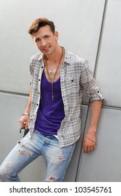 Smiling Young Freak Man Wearing Ripped Jeans Stands Near Gray Wall