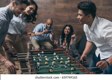 Smiling young friends playing table football together indoors  - Powered by Shutterstock