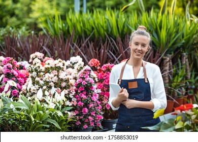 Smiling young gardener. Florists woman working with flowers in a greenhouse. Young woman working in flower garden. Woman entrepreneur. The young woman in a greenhouse - Powered by Shutterstock