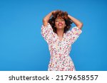 Smiling young girl with afro hairstyle and glamour makeup posing in floral dress on blue studio background, looking at the camera. A lot of copy space.