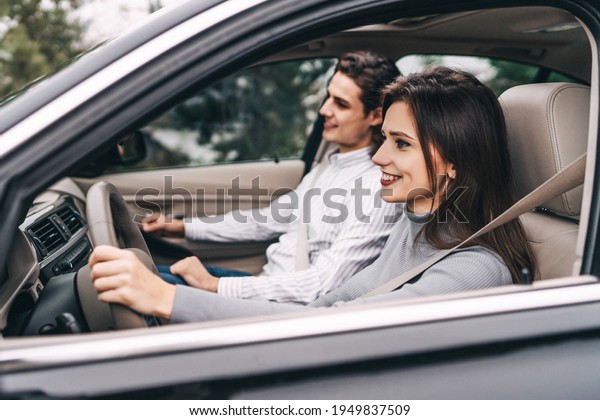 Smiling young girl behind the wheel,\
in front of her smiling young guy, road, car,\
comfort.