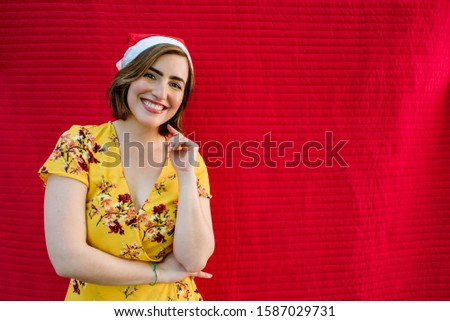 smiling young girl with christmas hat and yellow dress on a red background