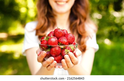 Smiling young girl holds a bowl of ripe freshly picked strawberries in her hands. Harvest strawberries. Close-up. - Powered by Shutterstock