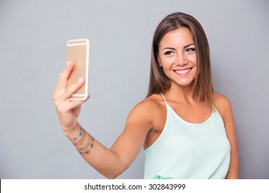 Mosolygó fiatal lány, így selfie fotó okostelefon felett szürke háttér