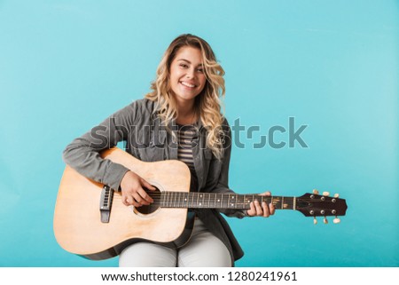 Smiling young girl playing a guitar while sitting isolated over blue