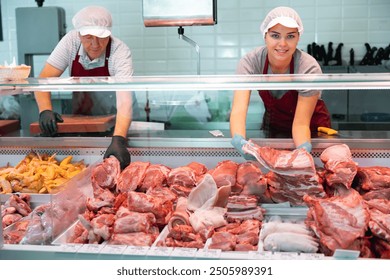 Smiling young girl, saleswoman of butcher shop, arranging meat products in glass display case, laying out slabs of fresh raw pork ribs - Powered by Shutterstock