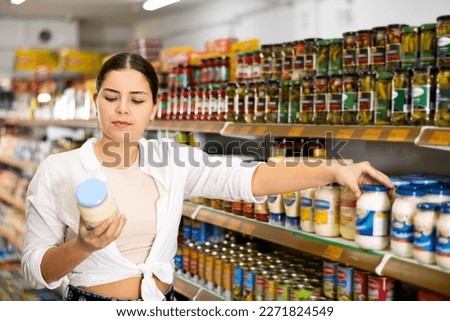 Smiling young girl shopping for groceries in supermarket, choosing light organic mayonnaise..