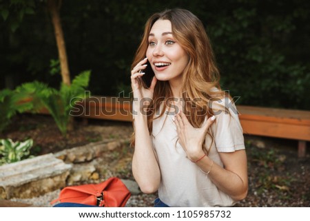 Smiling young girl talking on mobile phone while sitting on a bench outdoors