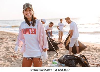 Smiling young girl volunteer cleaning beach from garbage with group of people volunteers - Powered by Shutterstock