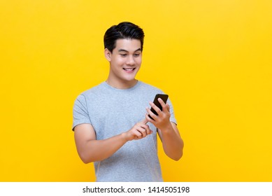 Smiling Young Good Looking Asian Man Using Smartphone To Get In Touch With Family And Friends Isolated On Bright Yellow Studio Background