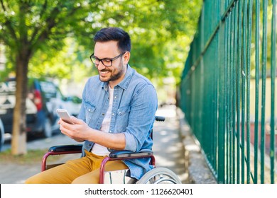 Smiling Young Handicapped Man In A Wheelchair Using Smart Phone