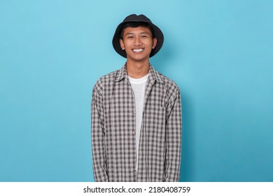 Smiling Young Handsome Asian Boy Using Flannel Shirt And Bucket Hat Standing Over Isolated Blue Background.