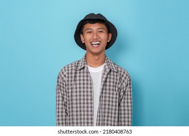 Smiling Young Handsome Asian Boy Using Flannel Shirt And Bucket Hat Standing Over Isolated Blue Background.