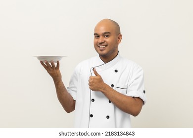 Smiling Young Handsome Asian Man Chef In Uniform Holding Empty Plate Delicious Dish Menu Good Taste On Isolated. Cooking Indian Man Occupation Chef Or Baker People In Kitchen Restaurant And Hotel.